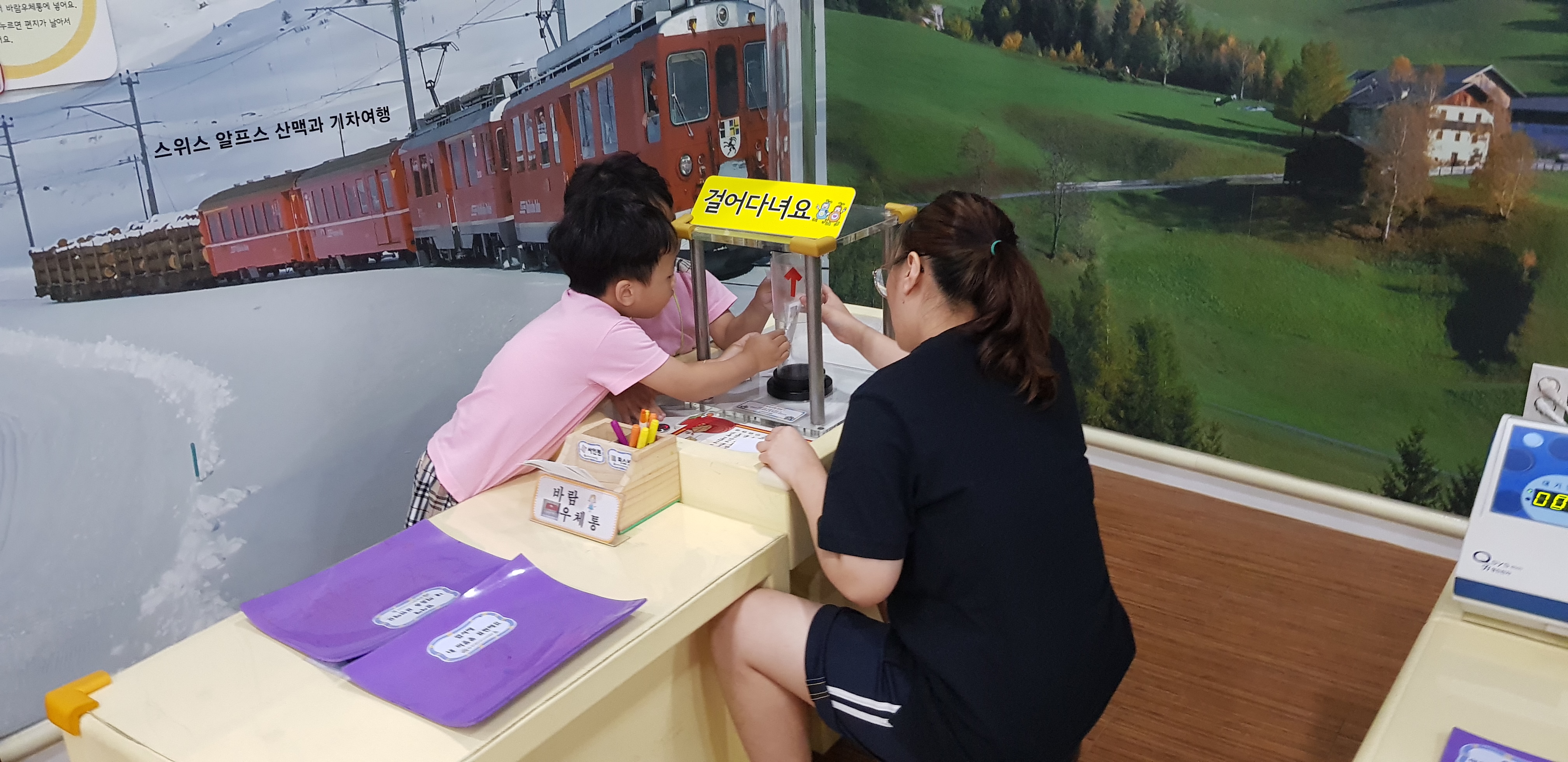스위스 알프스 산맥과 기차여행 걸어다녀요 푯말에 모여서 체험하고있는 유아들과 도와주는 고등학생