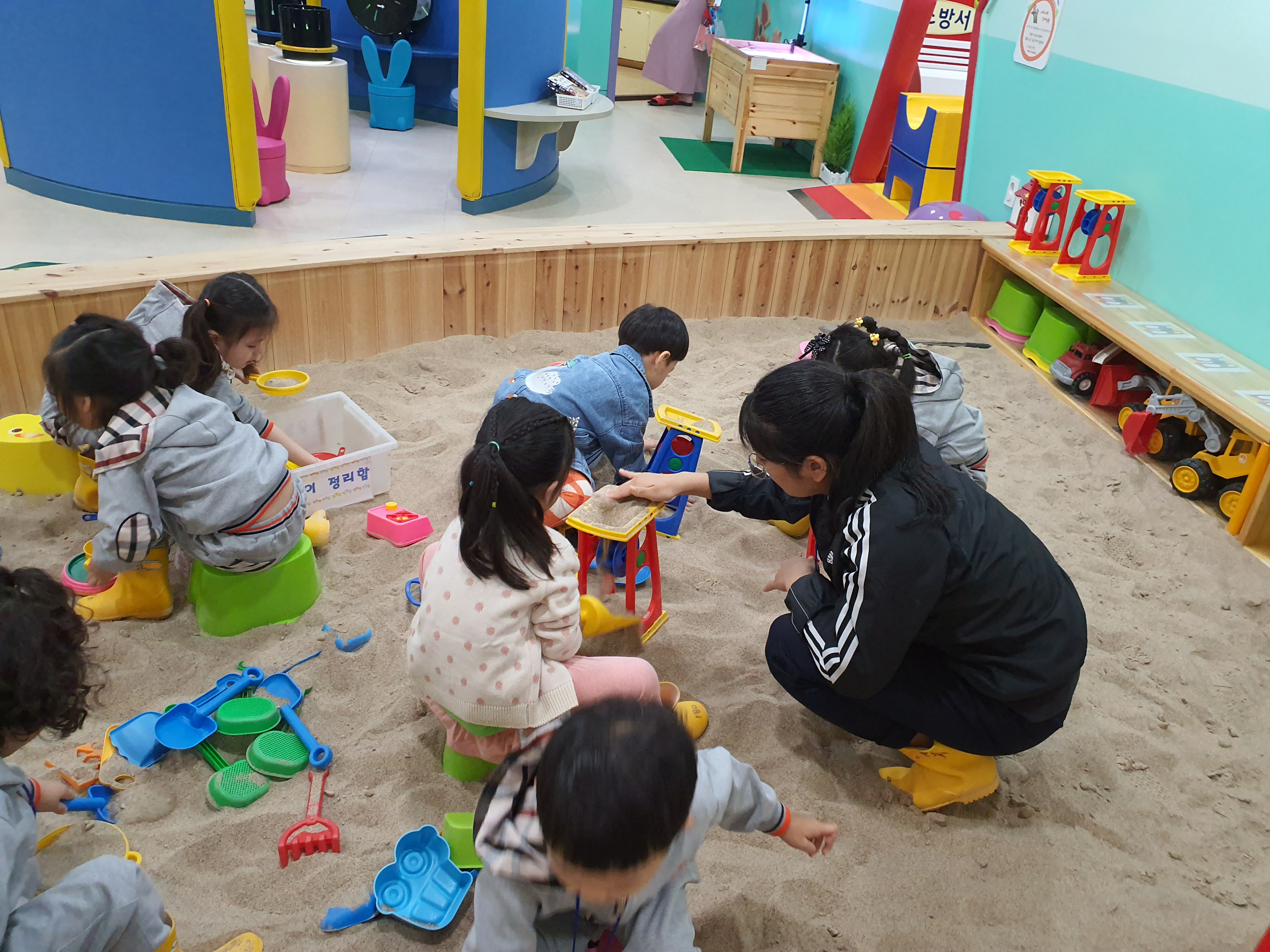 모래놀이하고있는 유아들과 도와주는 여중생
