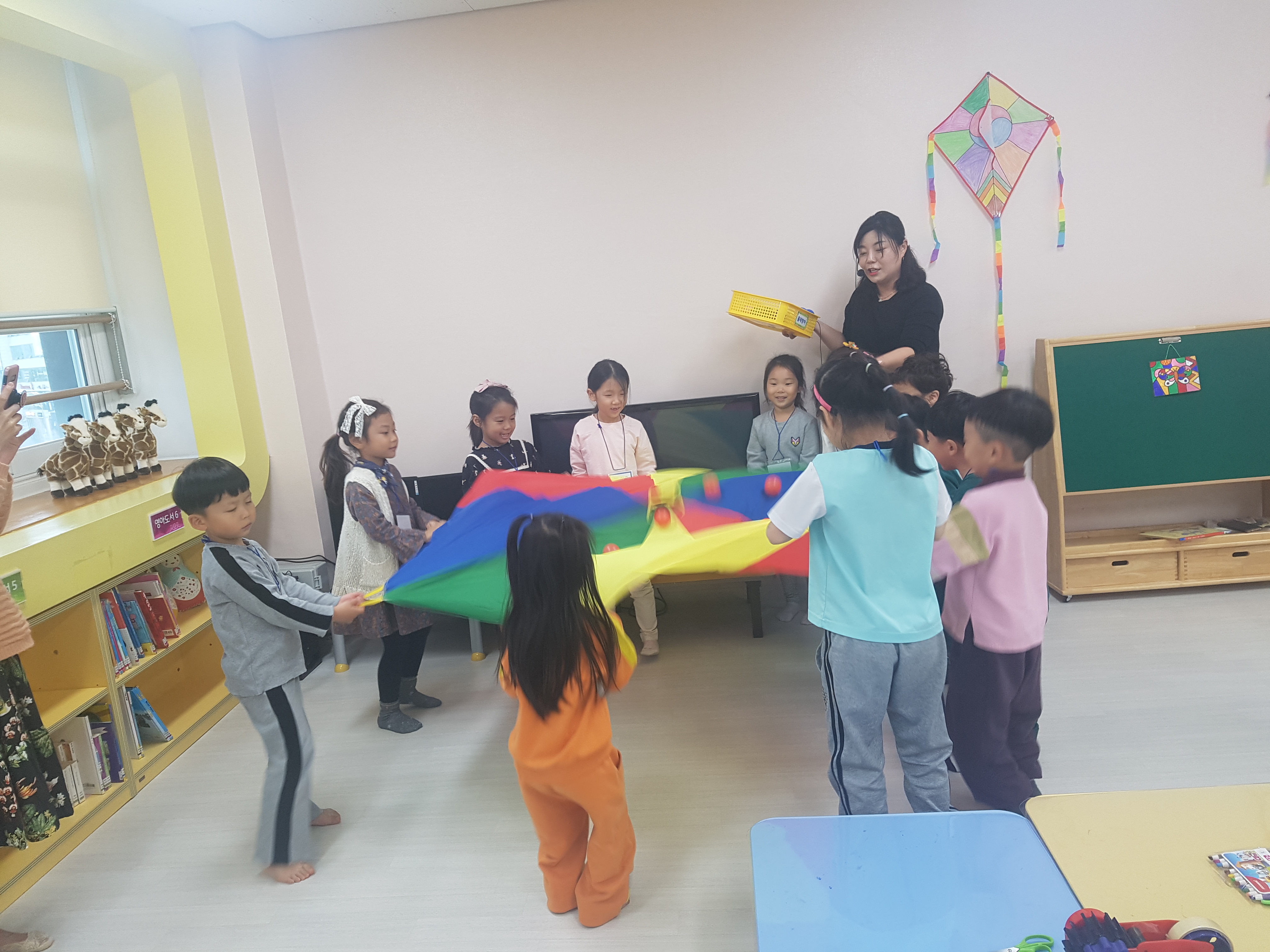 아이들이 모여서 보자기를 같이 펼치고 있고 그걸 설명해주는 선생님
