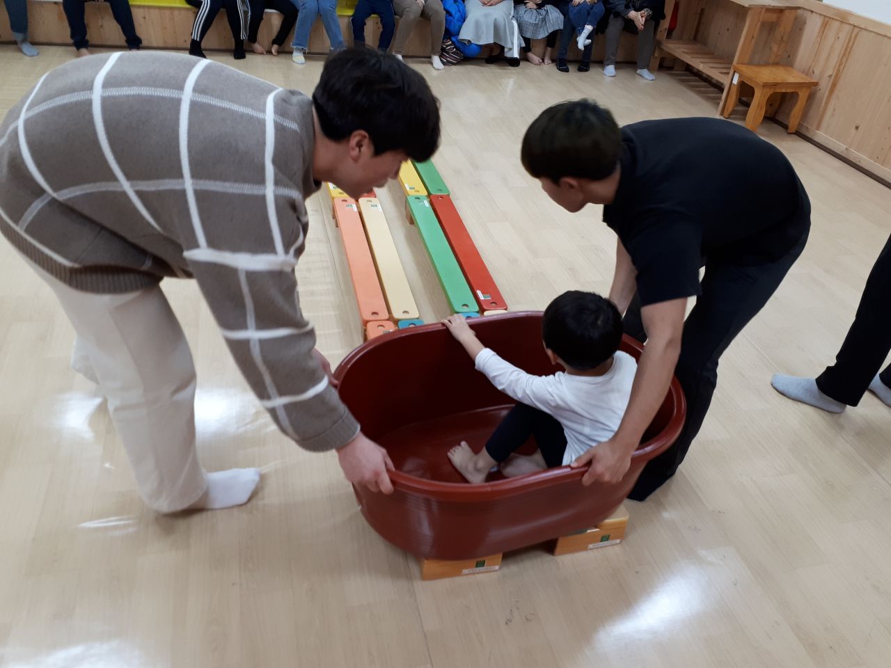 고무대야 에 앉아있는 아이와 그걸 끌고있는 두 남성